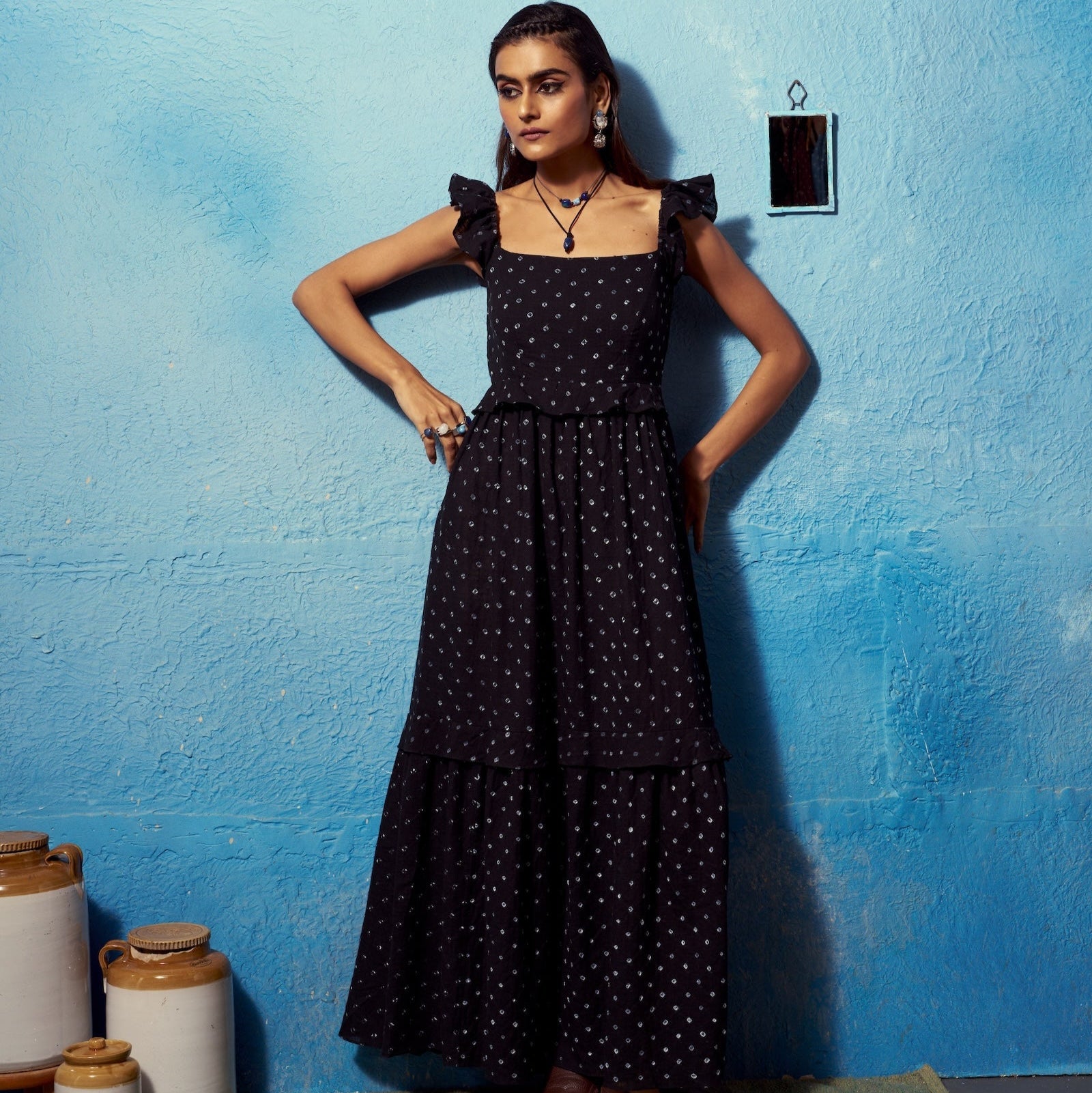 Woman in a black polka dot dress standing against a blue wall with jars on the floor.