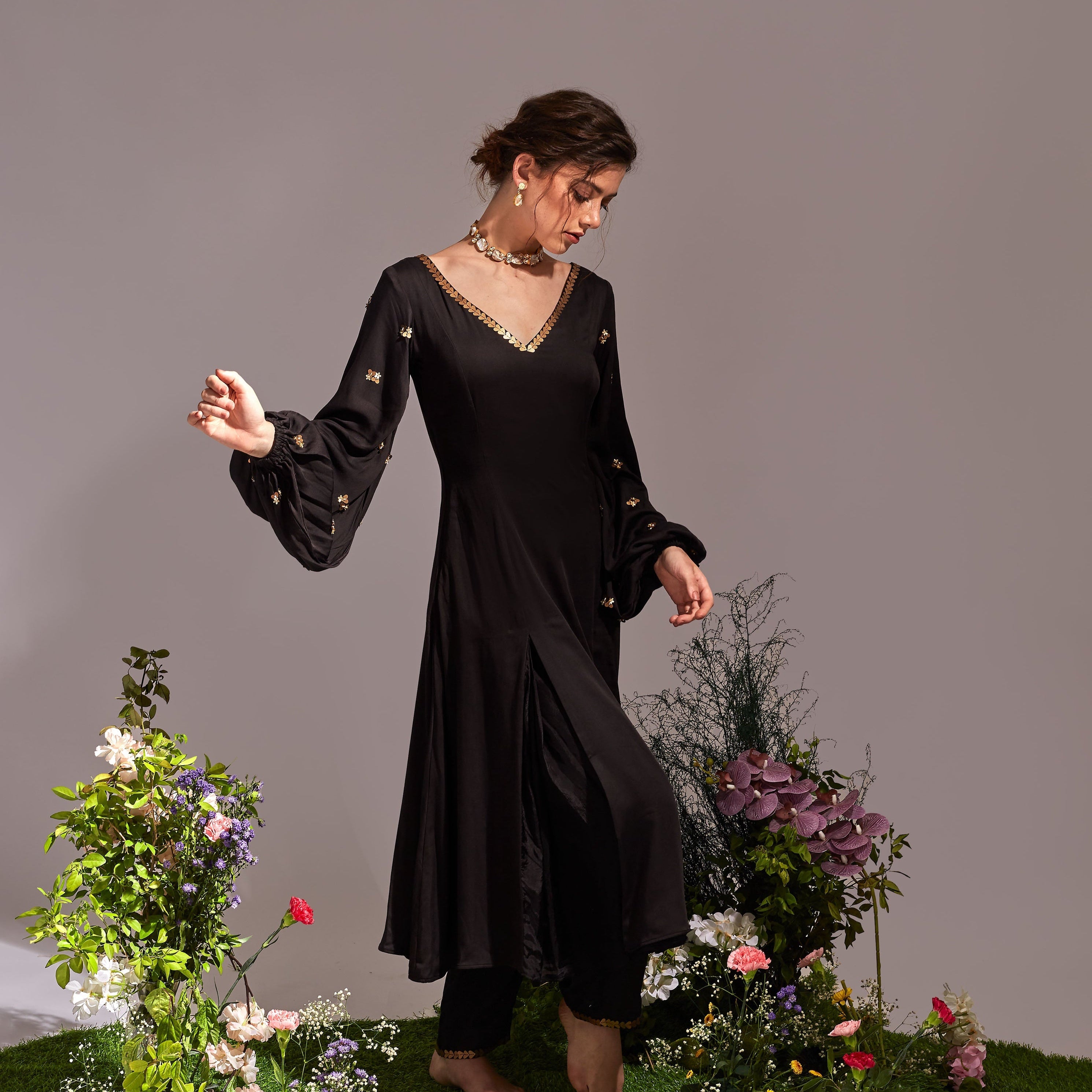 Woman in a black dress standing among flowers on a green platform with a gray background