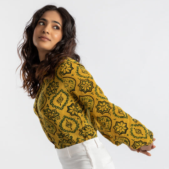 Woman wearing a mustard yellow patterned blouse against a white background