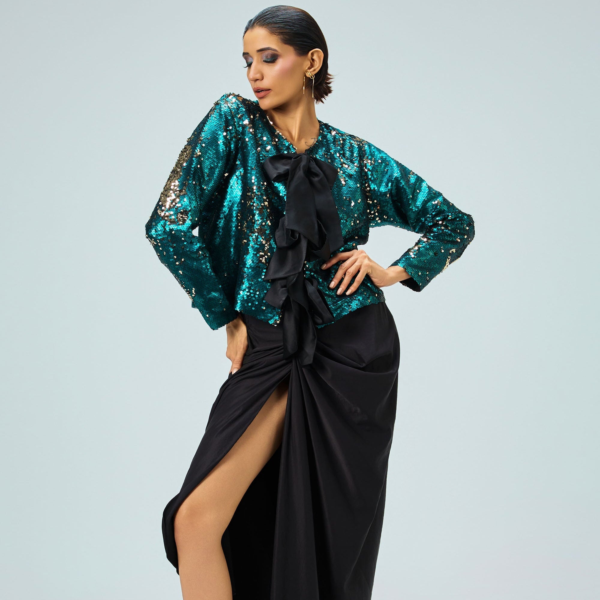 Woman wearing a teal sequin top and black skirt on a light gray background