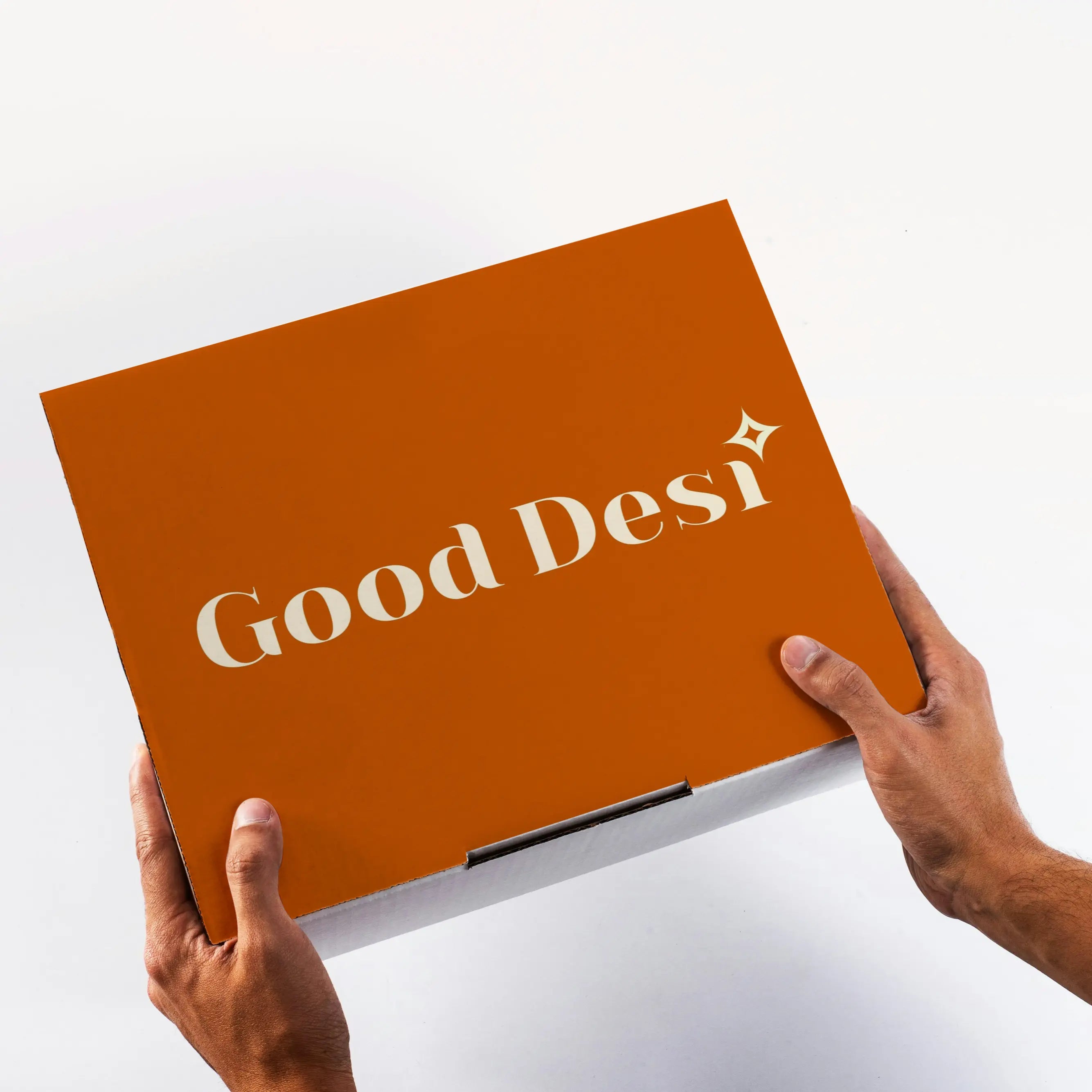 Person holding an orange box with 'Good Desi' branding on a white background