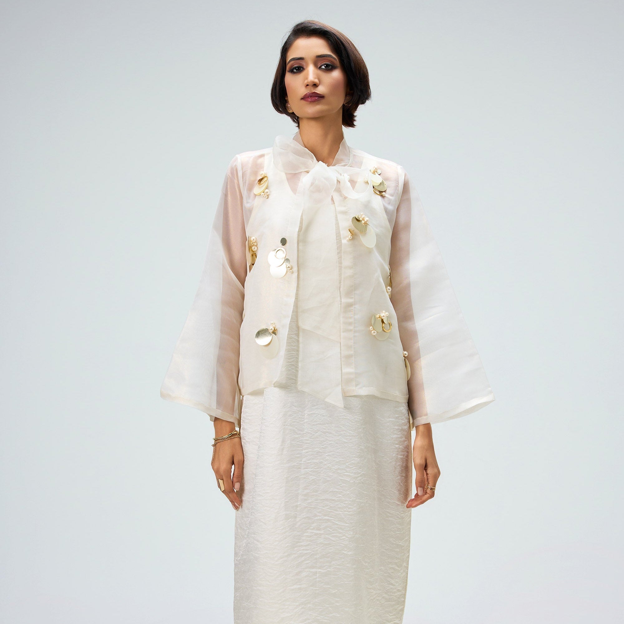 Woman wearing a white outfit with floral details on a plain background