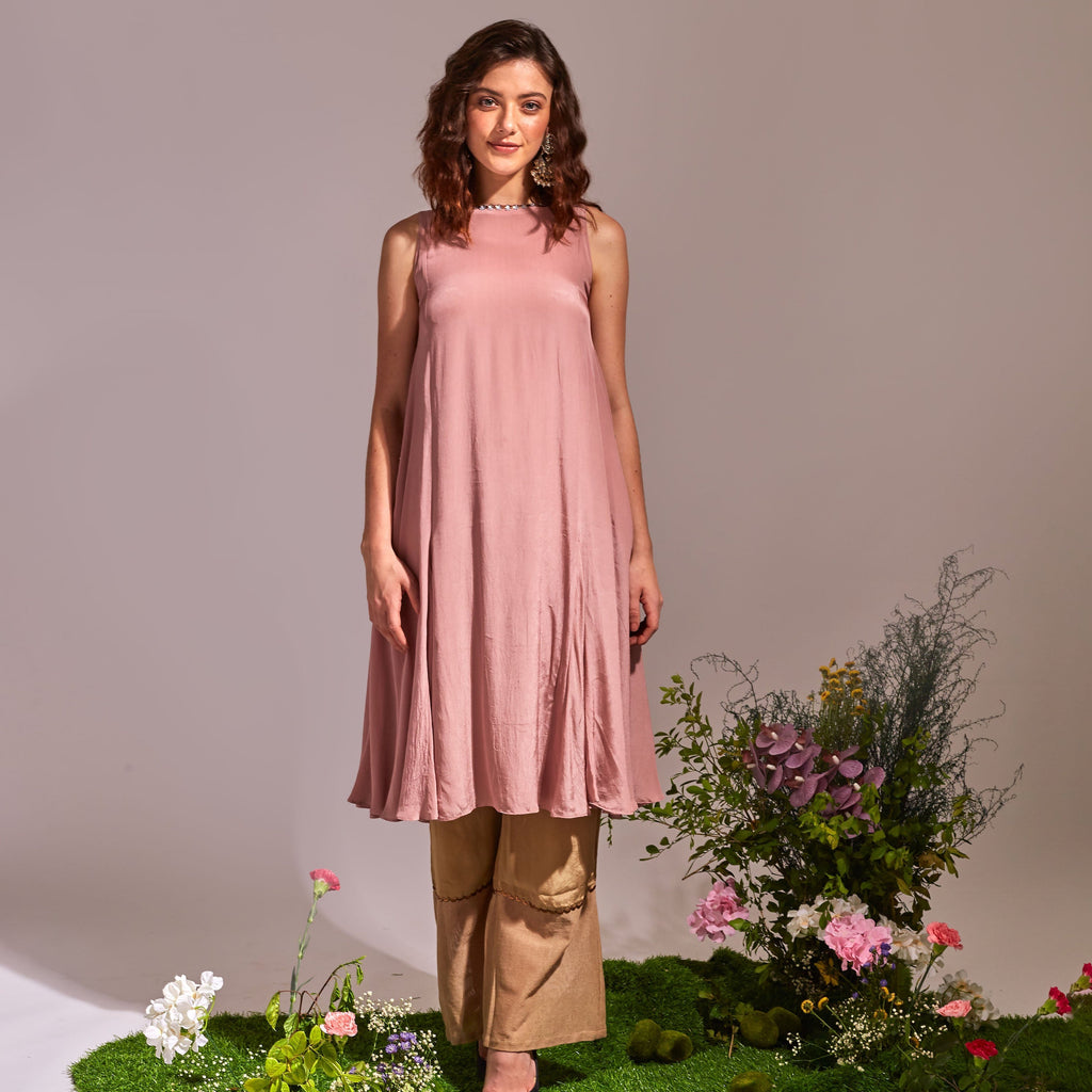 Woman in a pink dress standing on a grassy patch with flowers and plants around her.