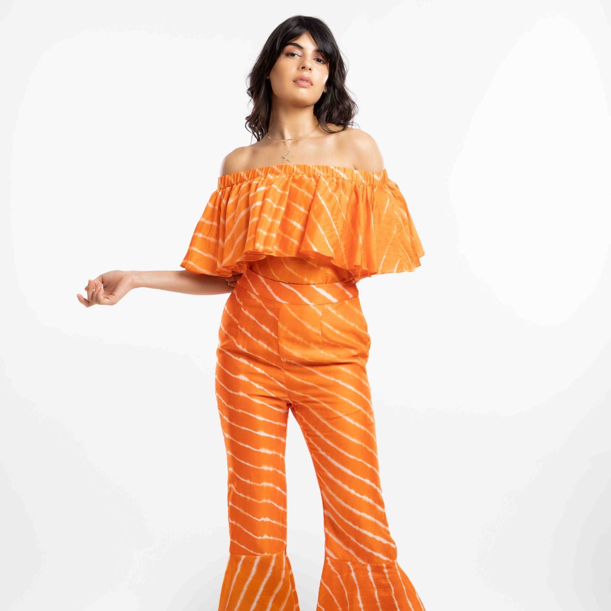 Woman wearing an orange off-shoulder top and striped pants on a white background