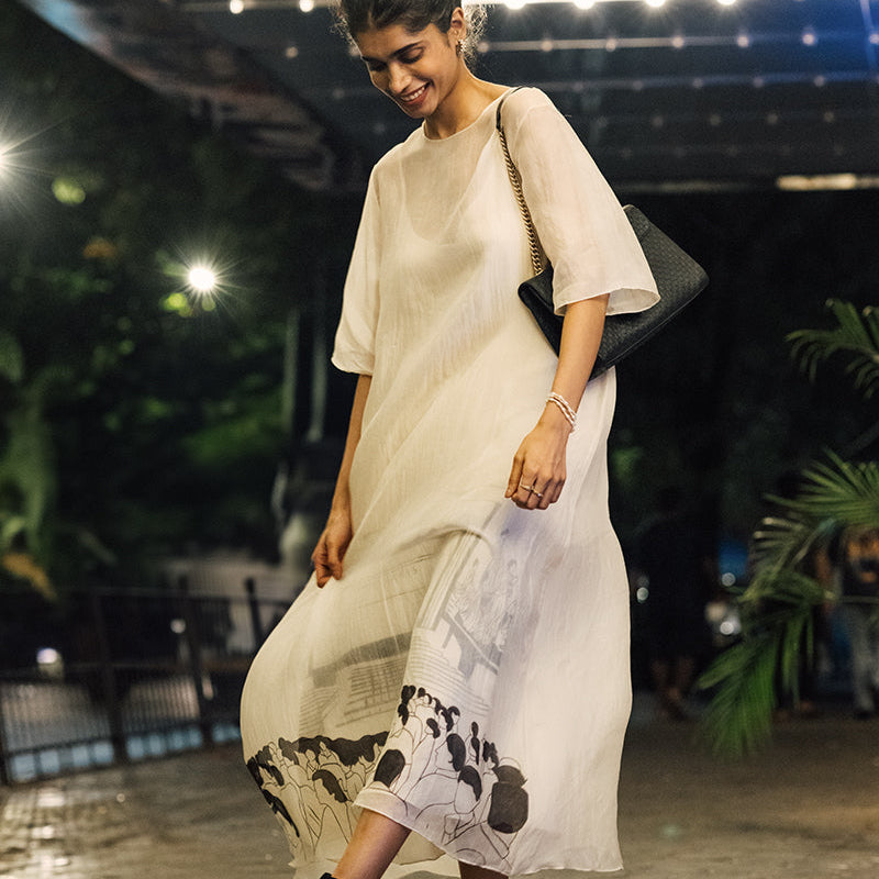 Woman in a beige dress with a floral pattern walking on a paved surface.